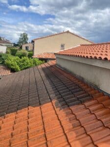 Toit en tuiles sales avant/après nettoyage: côté gauche sombre et mousseux, droit orange vif et propre, sous ciel nuageux.