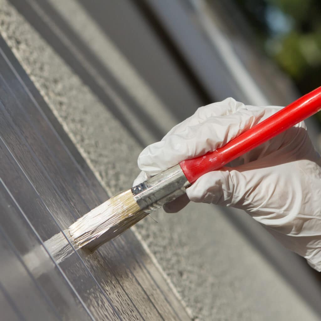 Main gantée de blanc appliquant de la peinture blanche avec un pinceau à une surface transparente striée en polycarbonate.