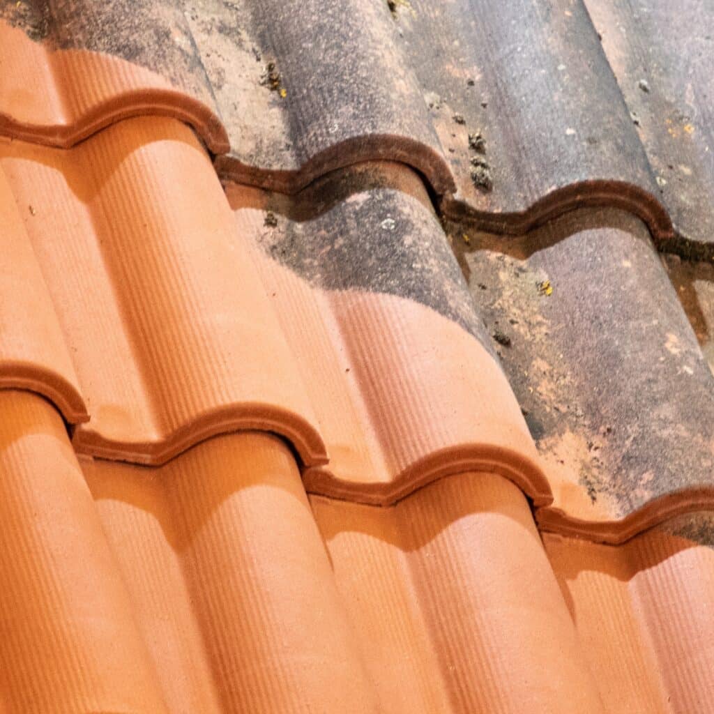 Tuiles de toit en terre cuite : moitié neuves, orange vif et lisses, moitié anciennes, grises et couvertes de mousse. Contraste nettoyage.